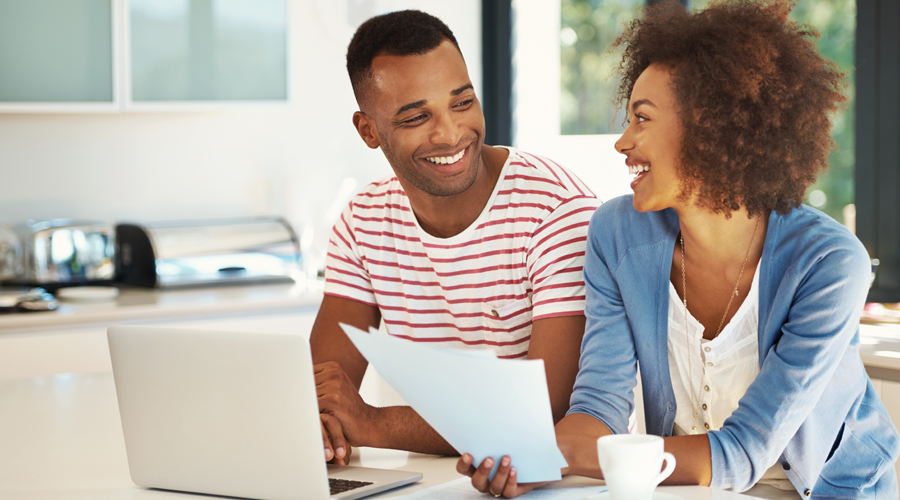 Happy, young couple reviewing paperwork and using laptop